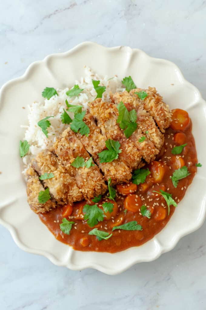 White plate with breaded pork, vegetable curry, rice and coriander