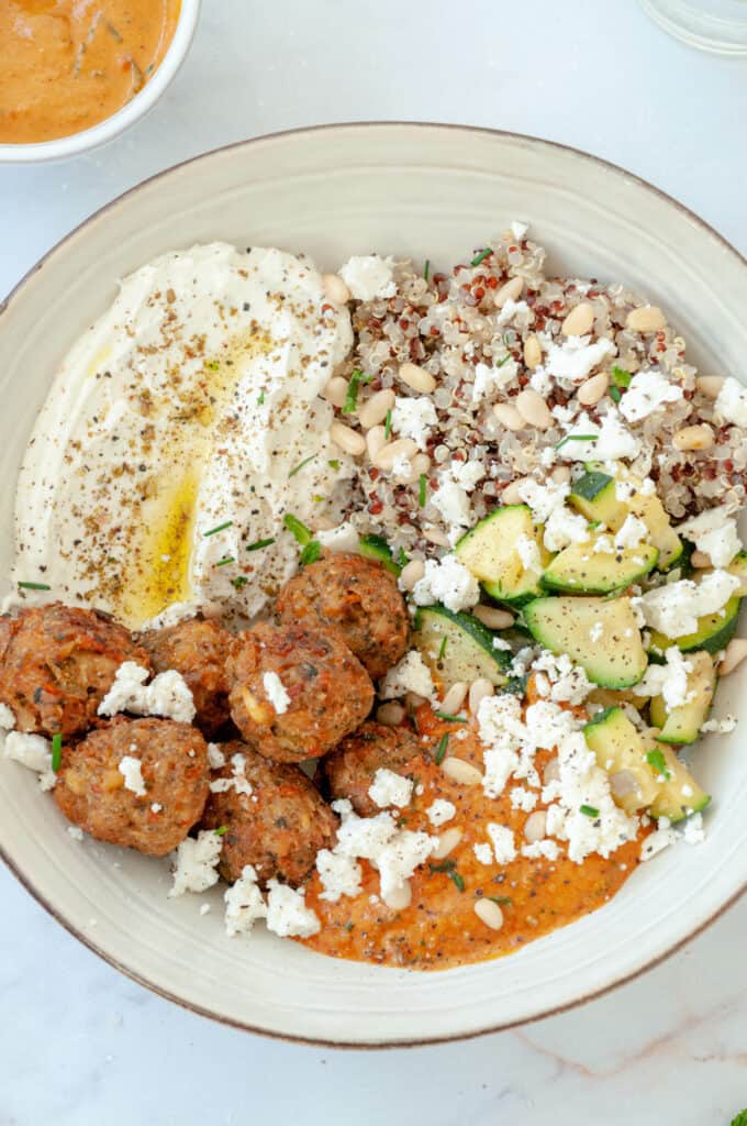 Zoom sur le bol de quinoa, falafels, labneh et courgettes, avec un pot de sauce au tahini.