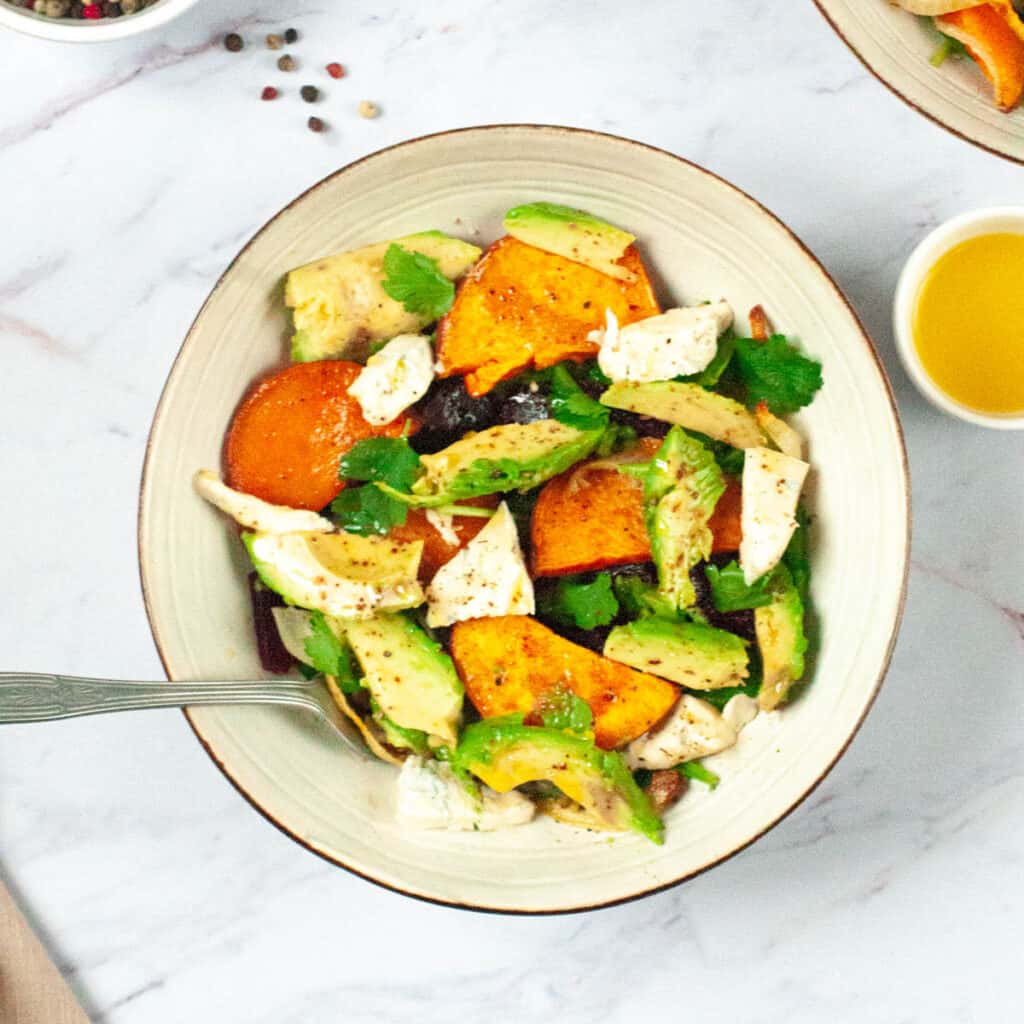 Sweet potato avocado salad in a white bowl, with gorgonzola and spinach.