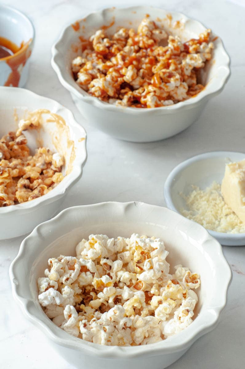 3 bowls of popcorn with a small bowl of caramel and another of cheddar.