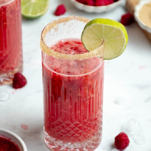 Bellini dans un verre avec une lamelle de citron vert et un bol de framboises.