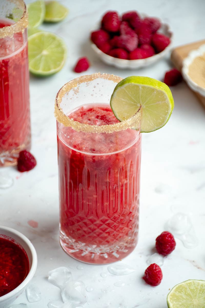 Bellini in a glass with a slice of lime and a bowl of raspberries.