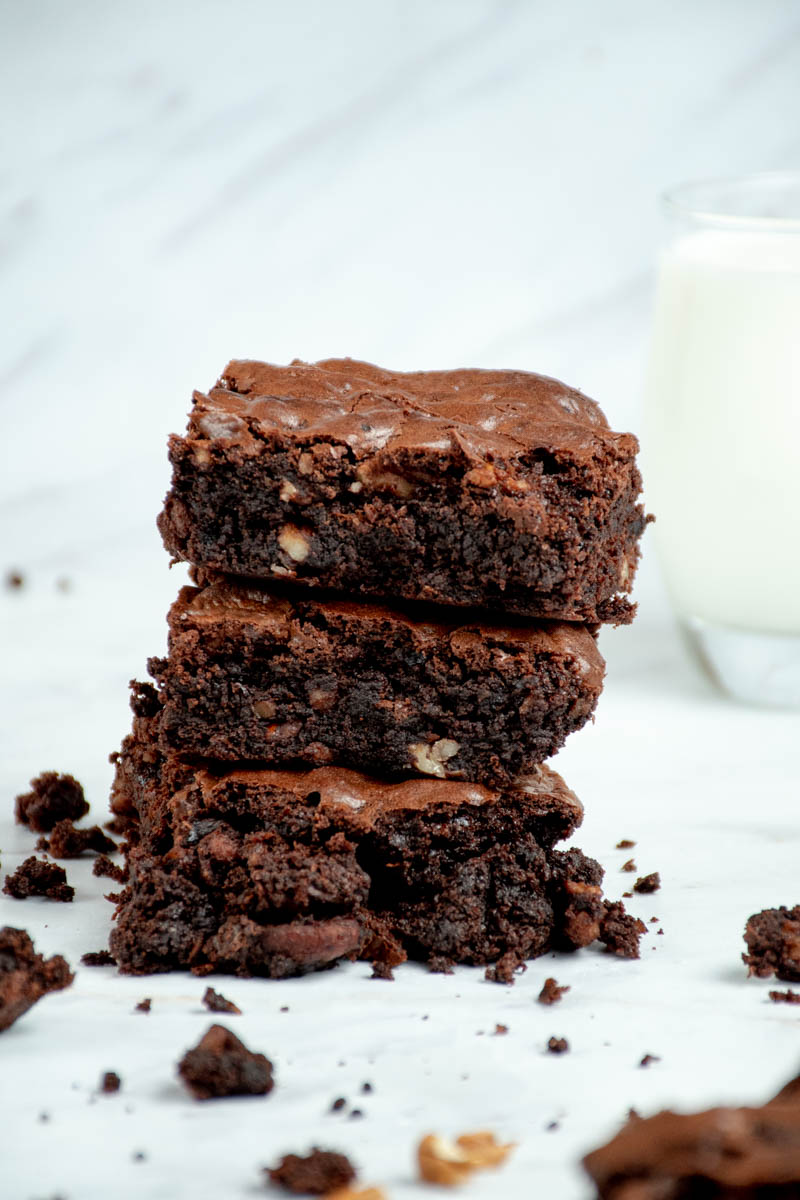 Pieces of walnut brownie stacked on top of each other, with a glass of milk.