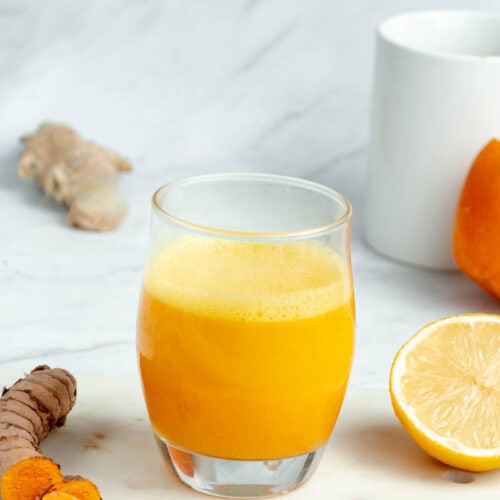 Ginger shot dans un verre avec un demi-citron et une racine de curcuma à côté.