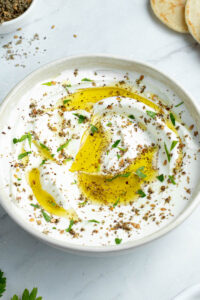 Labneh dans un bol beige avec de l'huile d'olive, du Zaatar et des feuilles de coriandre ciselée.