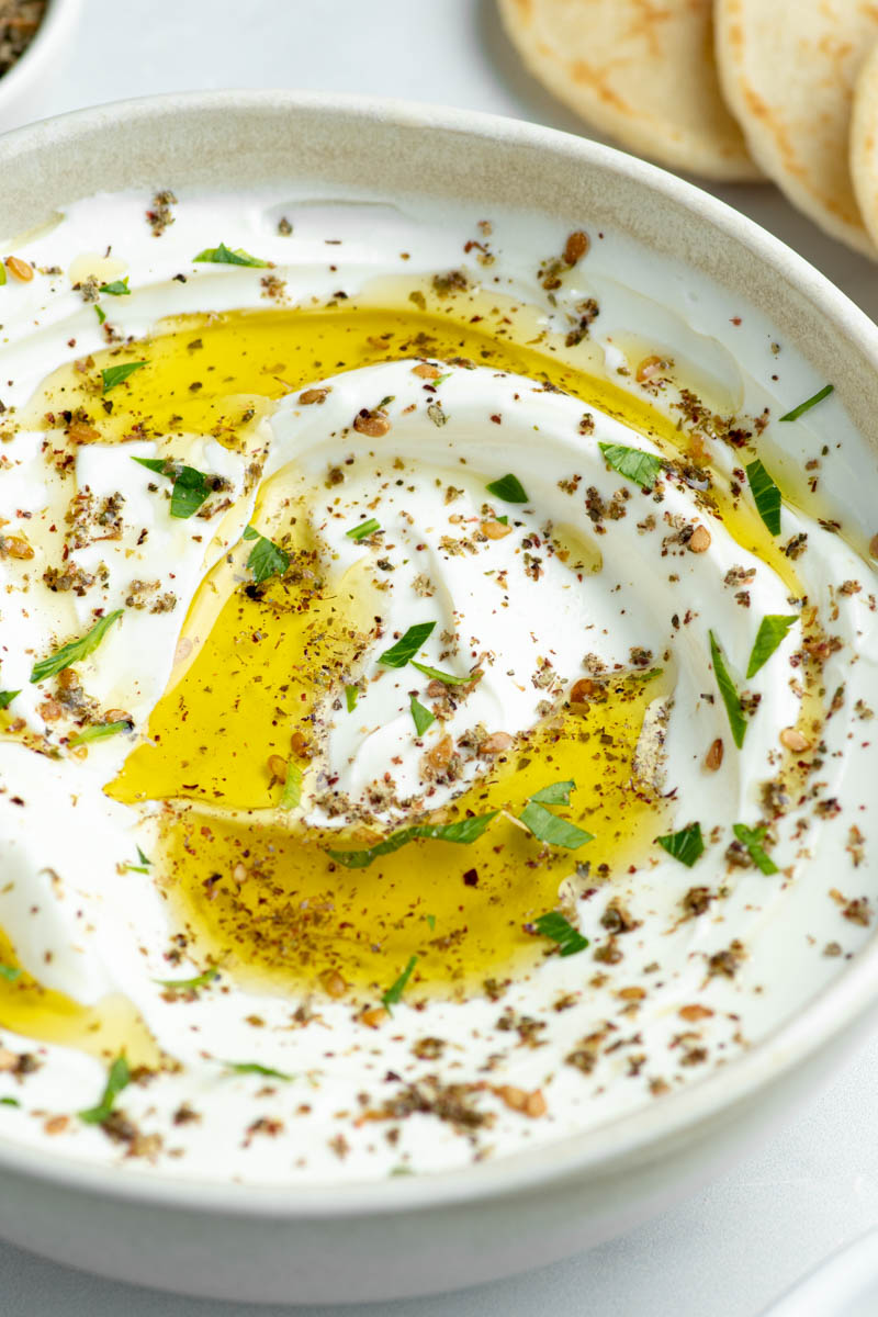 Labneh dans un bol beige avec de l'huile d'olive, du Zaatar et des feuilles de coriandre ciselée.