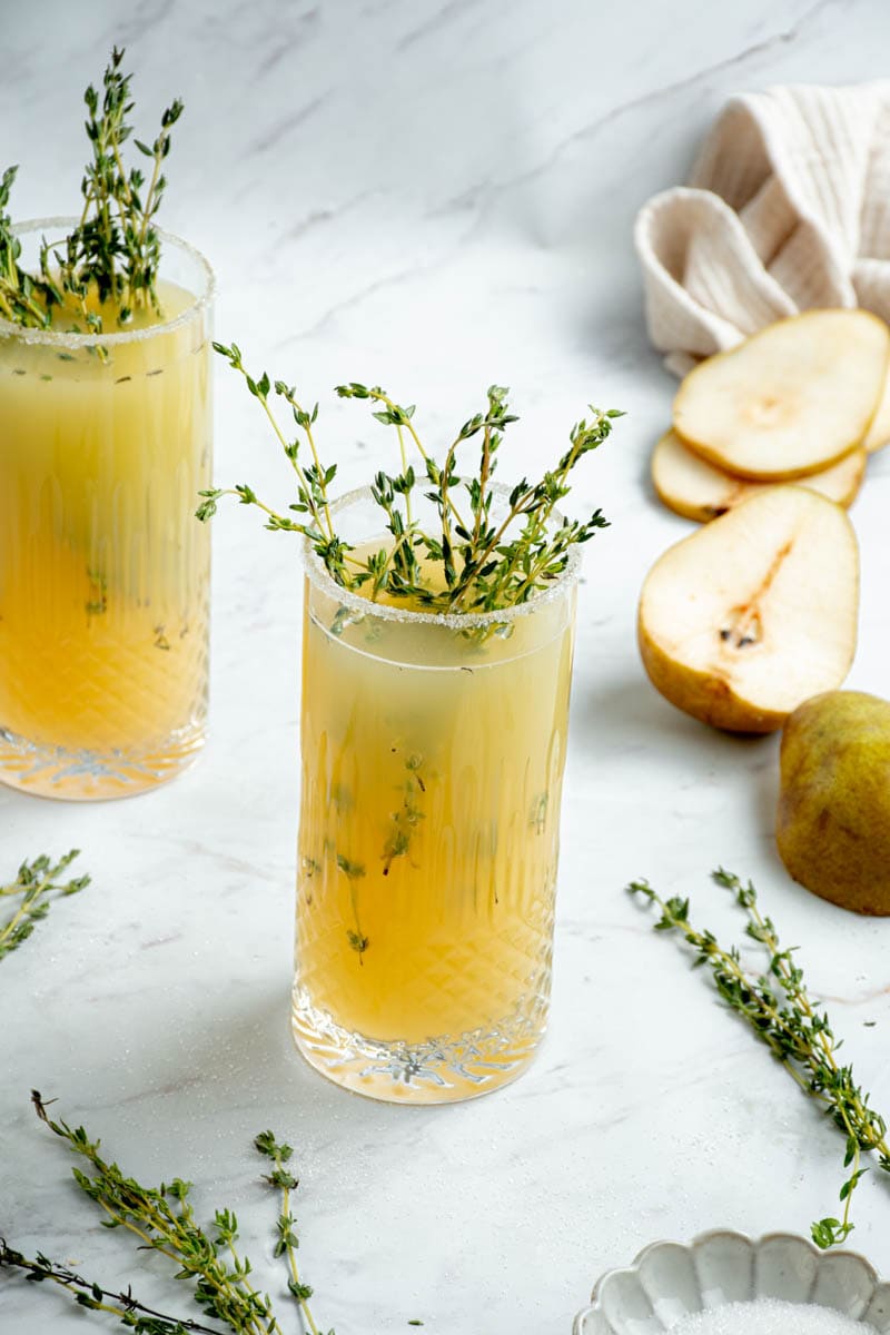 Pear and rose mocktail in two glasses, with thyme and pear halves.