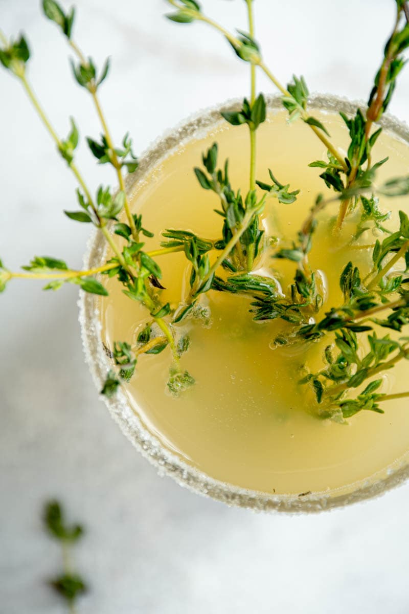 Mocktail poire et rose dans un verre, avec des branches de thym.