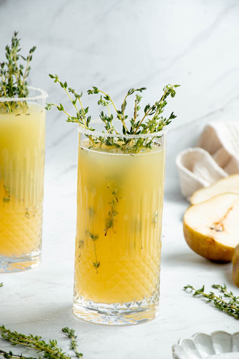 Pear and rose mocktail in two glasses, with thyme and pear halves.