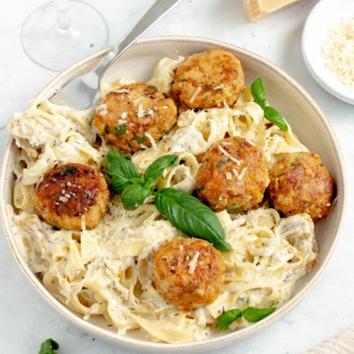 Boulettes de poulet dans une assiette avec des pâtes à la crème et des feuilles de basilic.