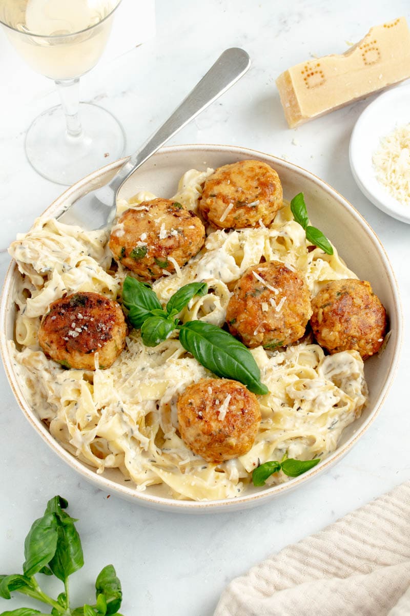 Chicken meatballs on a plate with creamy pasta and basil leaves.