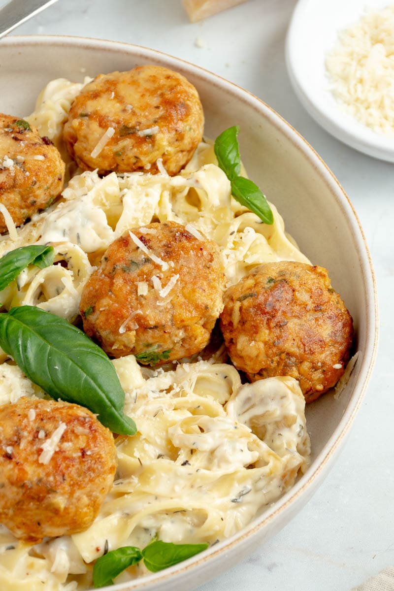 Chicken meatballs on a plate with creamy pasta and basil leaves.