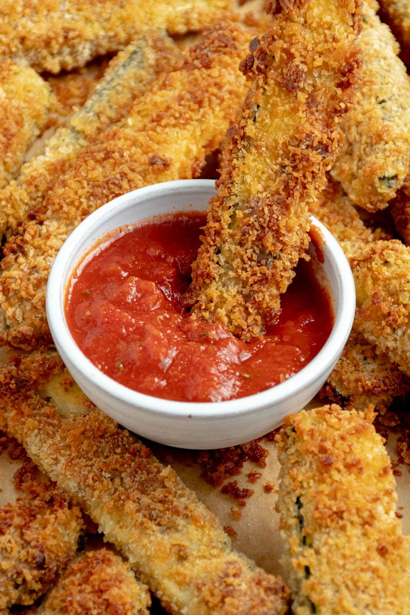 Fried zucchini dipped in a bowl of tomato sauce.
