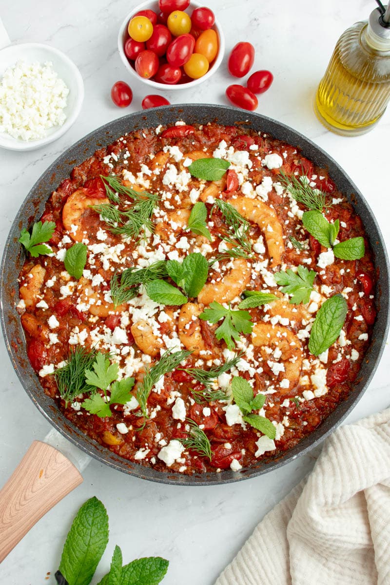 Shrimp saganaki in a pan with herbs and feta cheese.