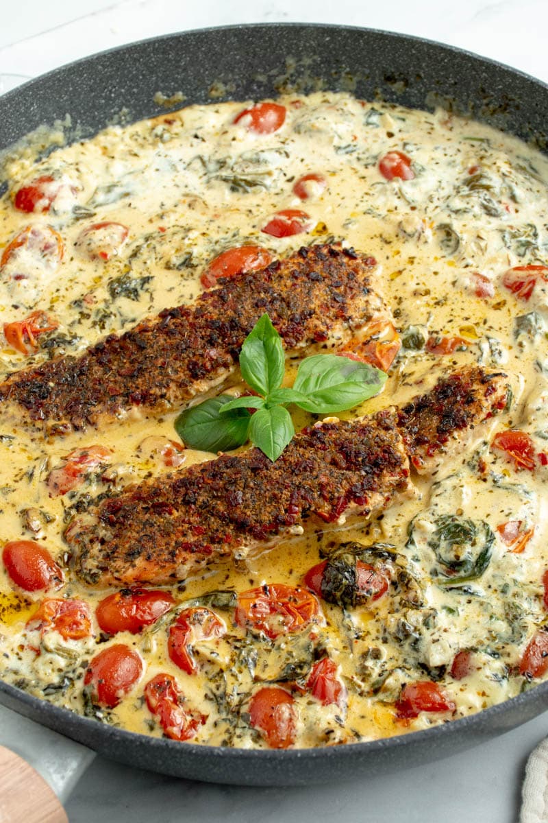 Two Tuscan-style salmon steaks in a frying pan, with fresh basil.
