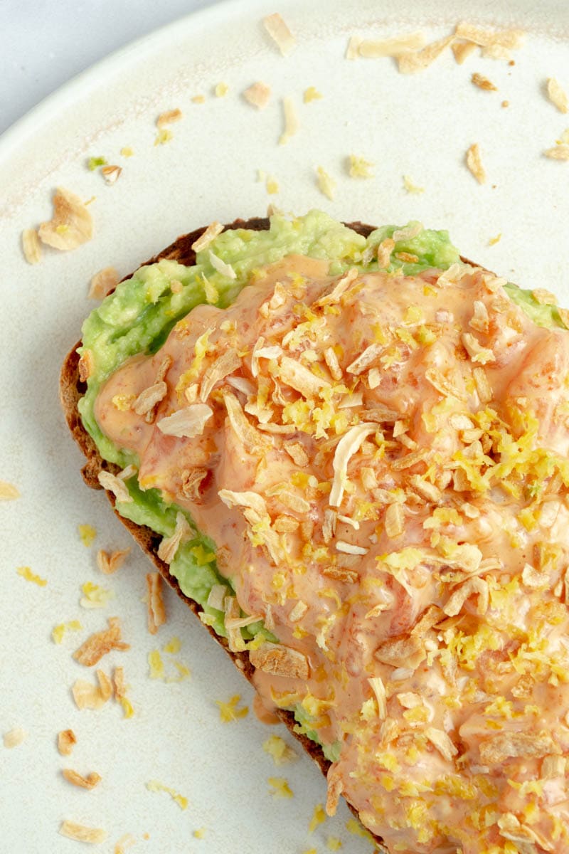 Avocado, salmon and spicy mayo toast on a plate.