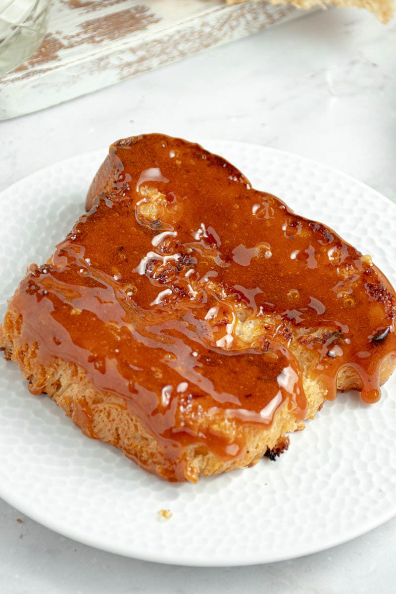 A slice of brioche perdu with a crunchy layer of caramel on a white plate.