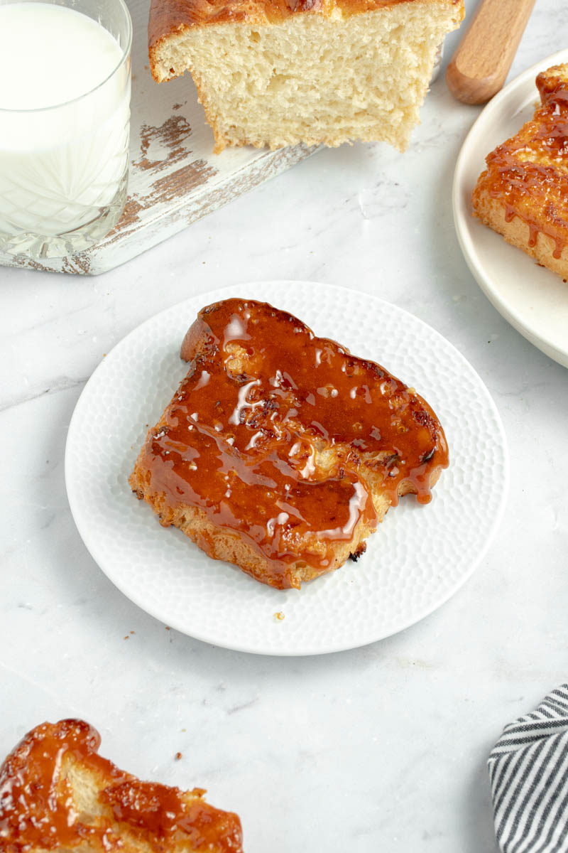 A slice of brioche perdu with a crunchy layer of caramel on a white plate and a glass of milk.