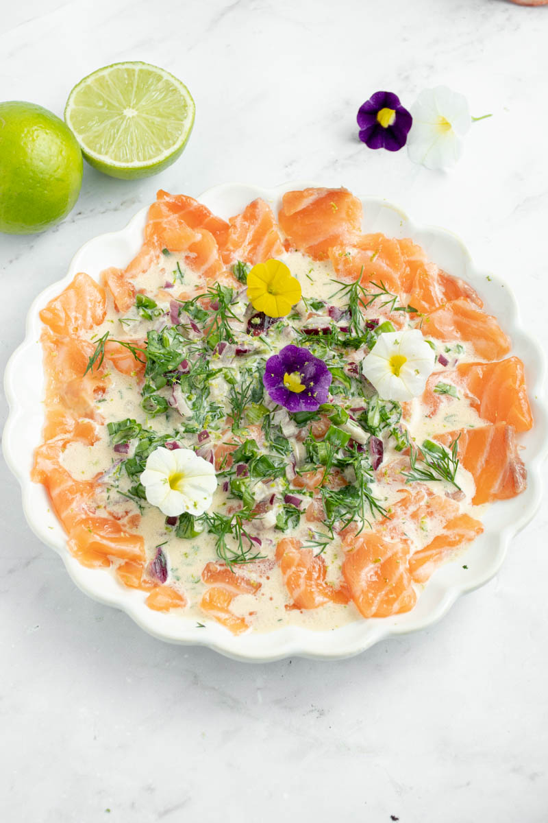 Crudo de saumon dans une assiette avec une sauce aux herbes et des fleurs comestibles.