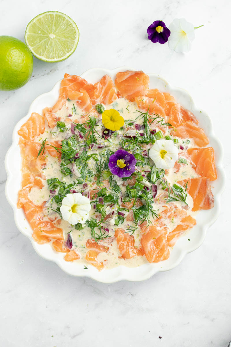 Salmon crudo on a plate with herb sauce and edible flowers.