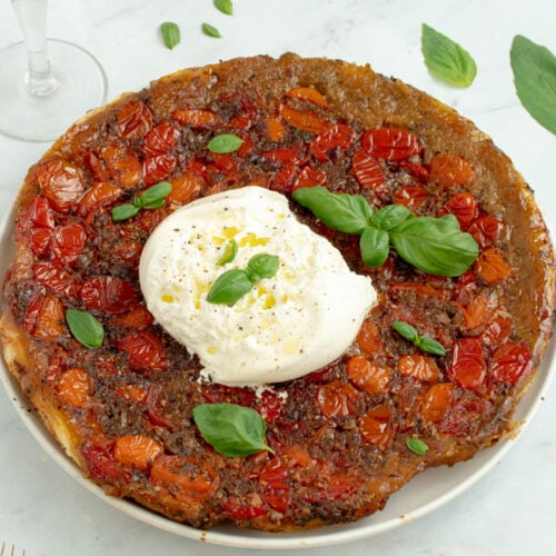 Tarte tatin de tomates cerises dans une assiette avec une burrata et des feuilles de basilic.