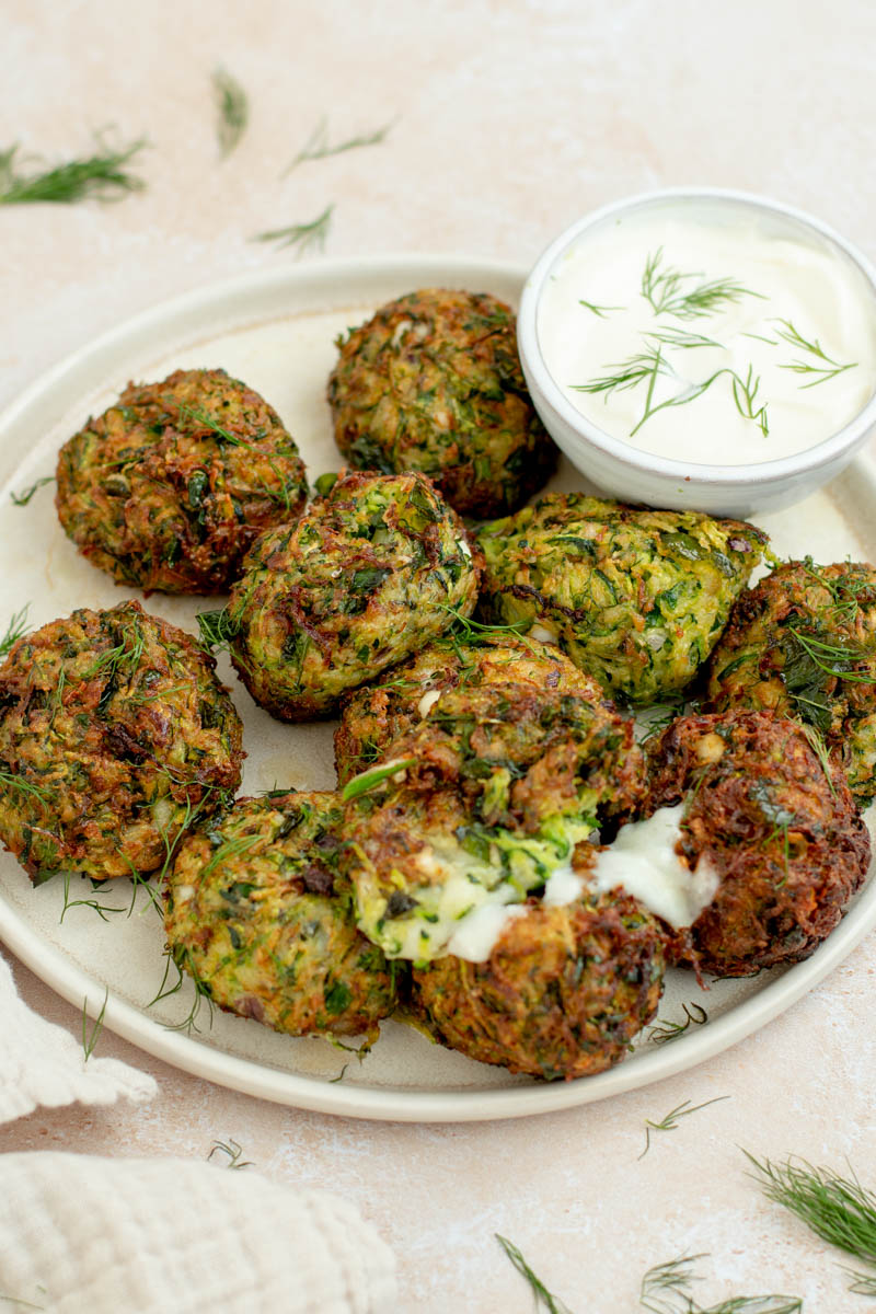 Zucchini croquettes on a plate with a bowl of sauce.
