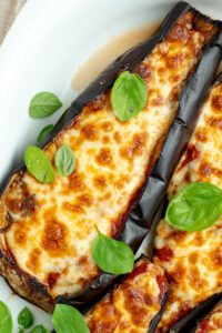 Half an eggplant in a white dish, covered with basil.