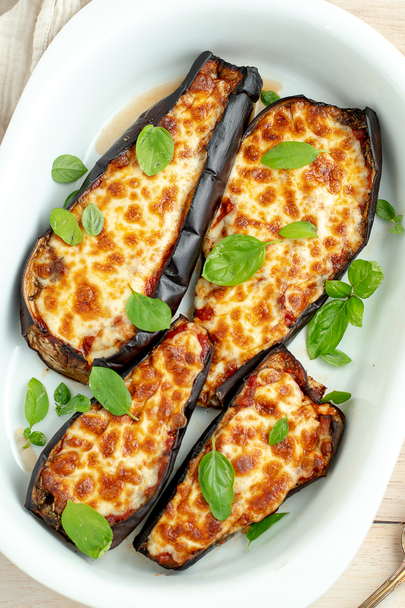 4 eggplant halves in a white dish, covered with basil.