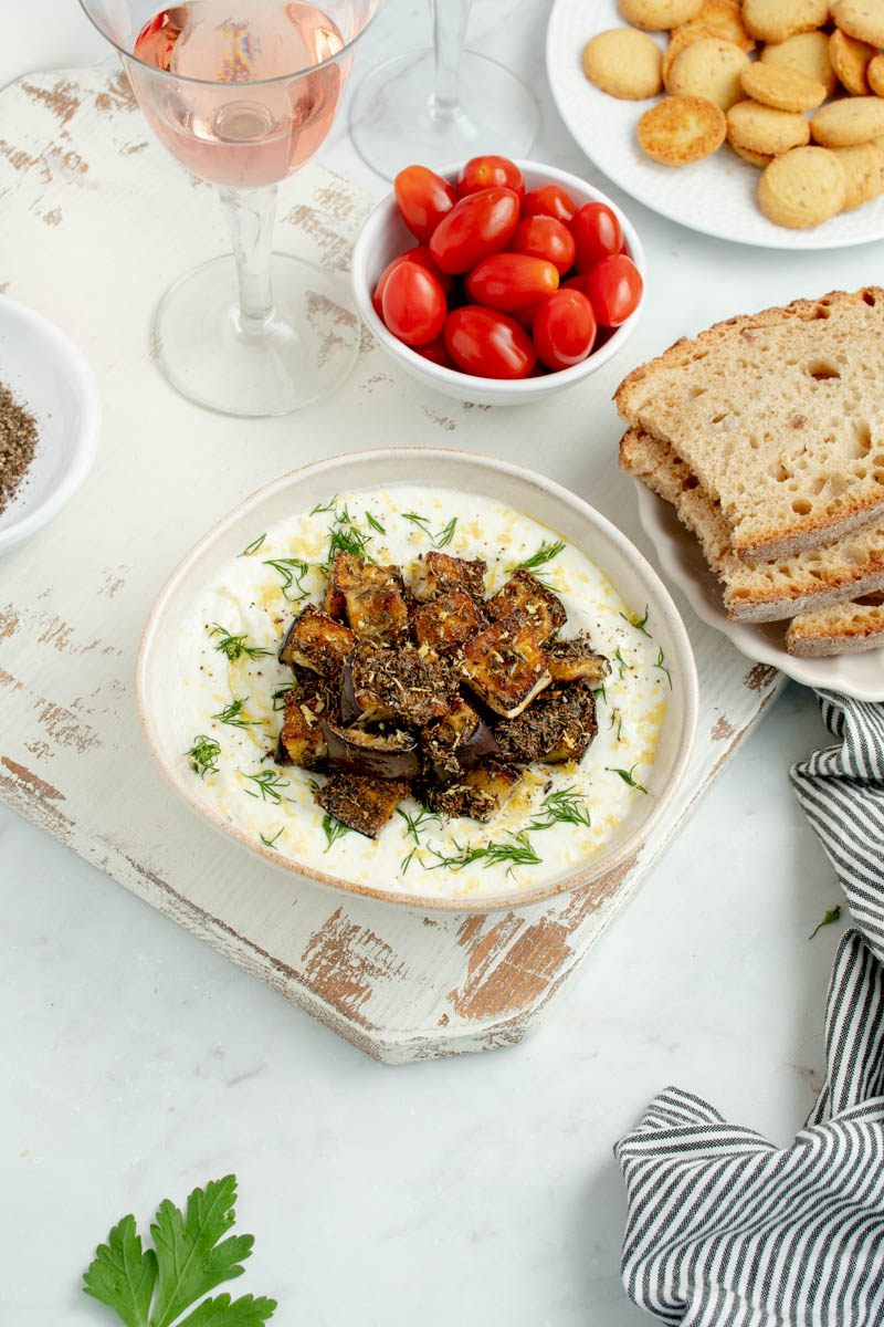 Cream of feta cheese in a white bowl with slices of bread and a bowl of cherry tomatoes.
