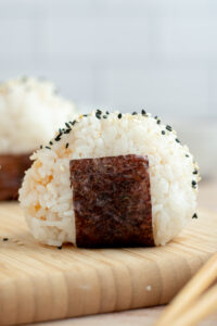 Onigiri with a Nori seaweed leaf and sesame seeds on a wooden board.