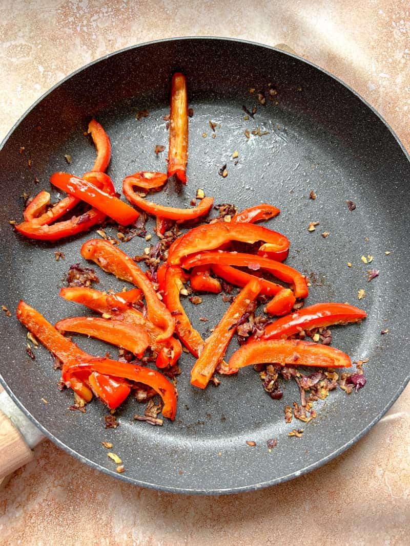 Red peppers, garlic and red onion cooked in a frying pan.