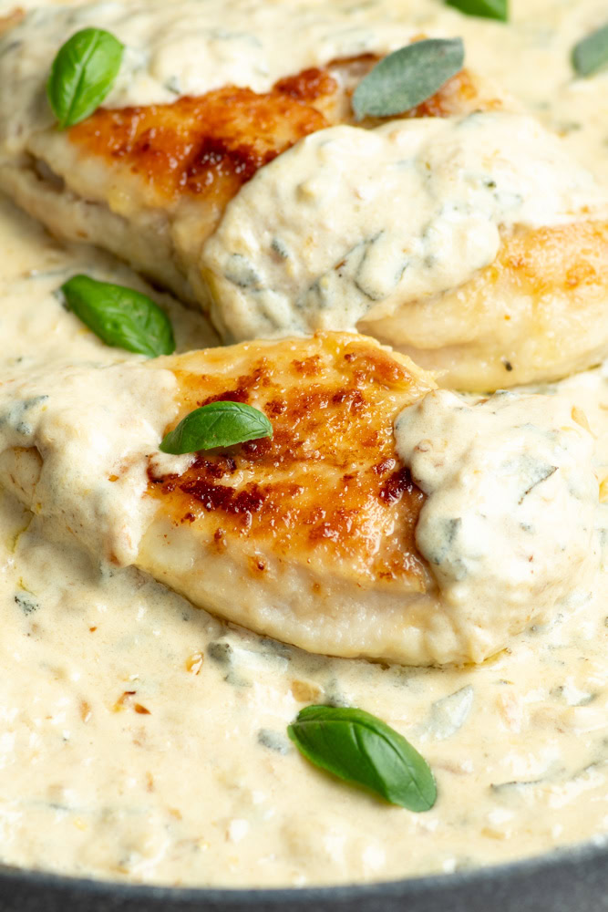 Two golden chicken fillets bathed in a lemon-sage cream sauce, with fresh basil leaves.