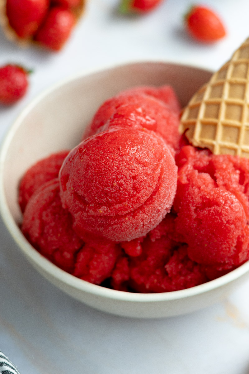 Several scoops of strawberry sorbet in a bowl, with ice cream cones.