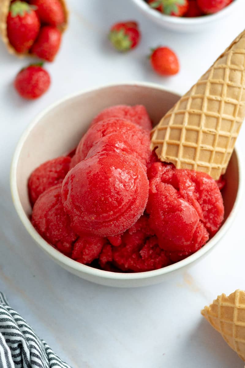Several scoops of strawberry sorbet in a bowl, with ice cream cones.