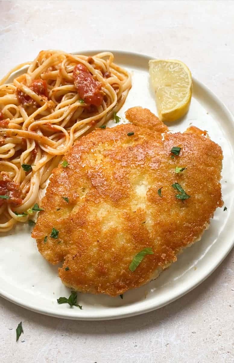 Crusted Romano chicken in a plate with tomato pasta.