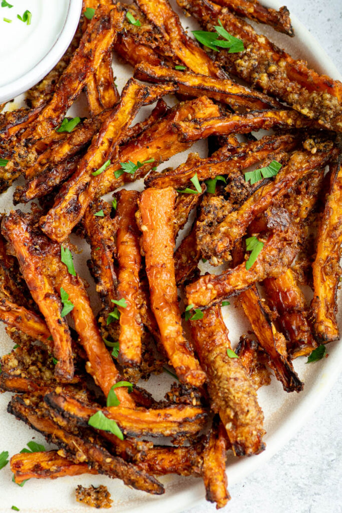 Air fryer carrot fries in a plate with fresh parsley and a bowl of sauce.
