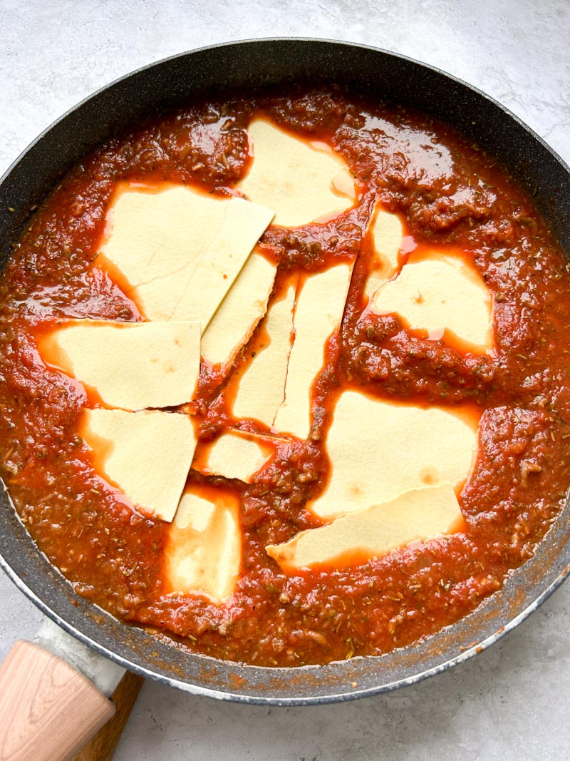 Feuilles de lasagnes cassées dans la sauce tomate, dans la poêle.
