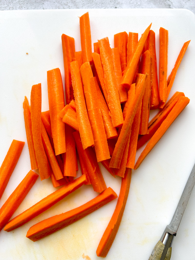 All carrots sticks on the white cutting board.