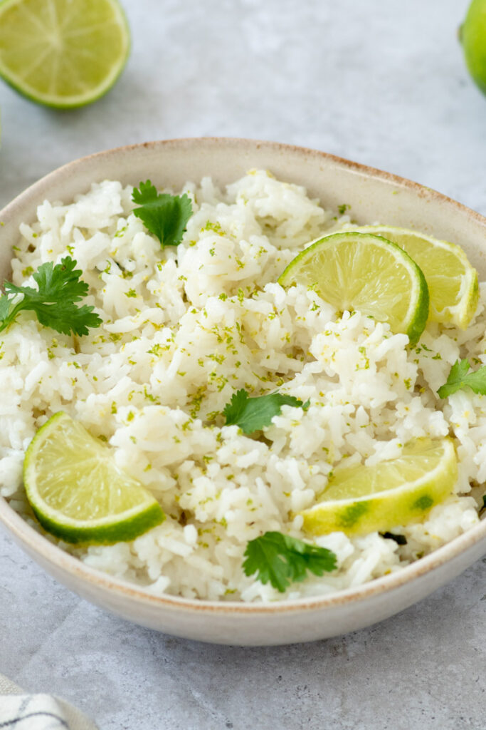 Coconut rice with lime wedges and fresh cilantro leaves in a beige bowl.