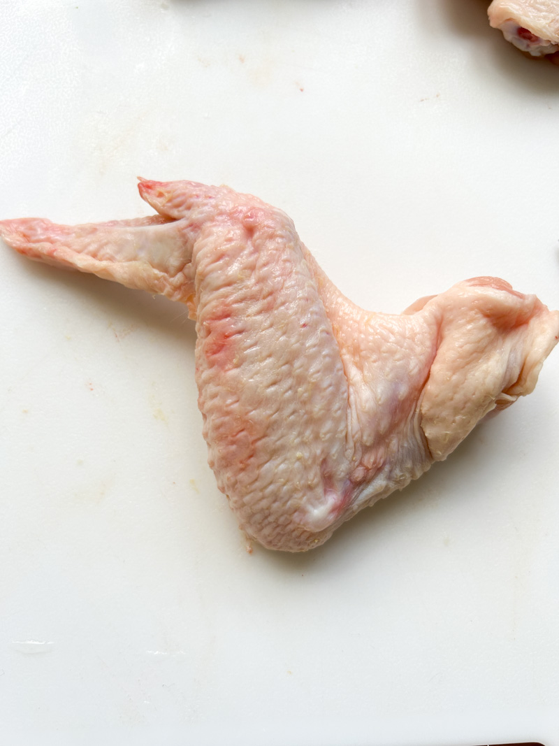 Aile de poulet entière sur une planche de découpe blanche.