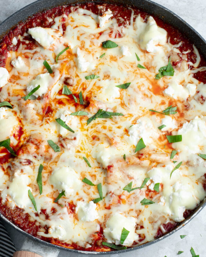 Deconstructed lasagna in a frying pan, with freshly chopped basil.