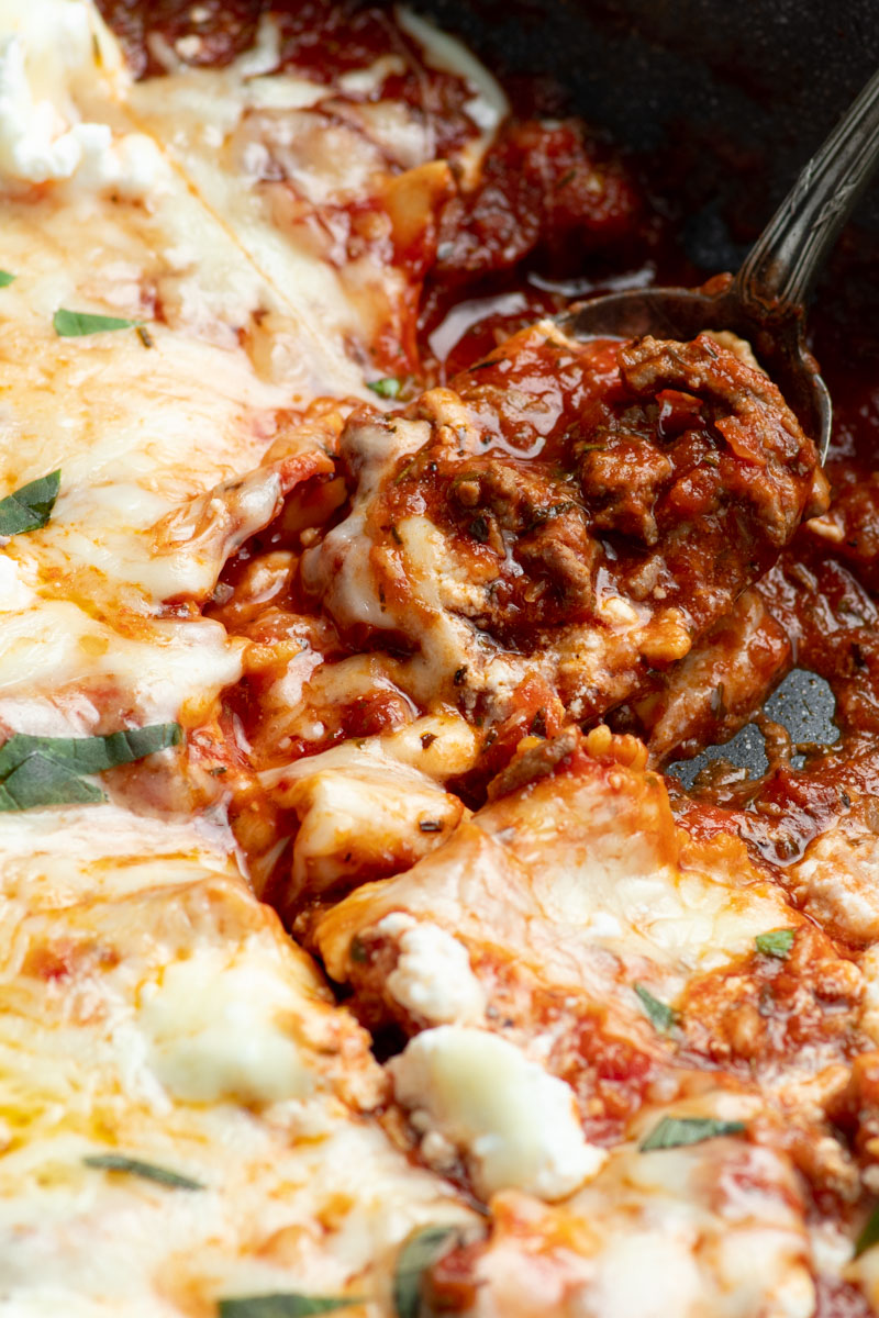 Une cuillère avec du boeuf haché, de la sauce tomate juteuse et des lasagnes dedans.