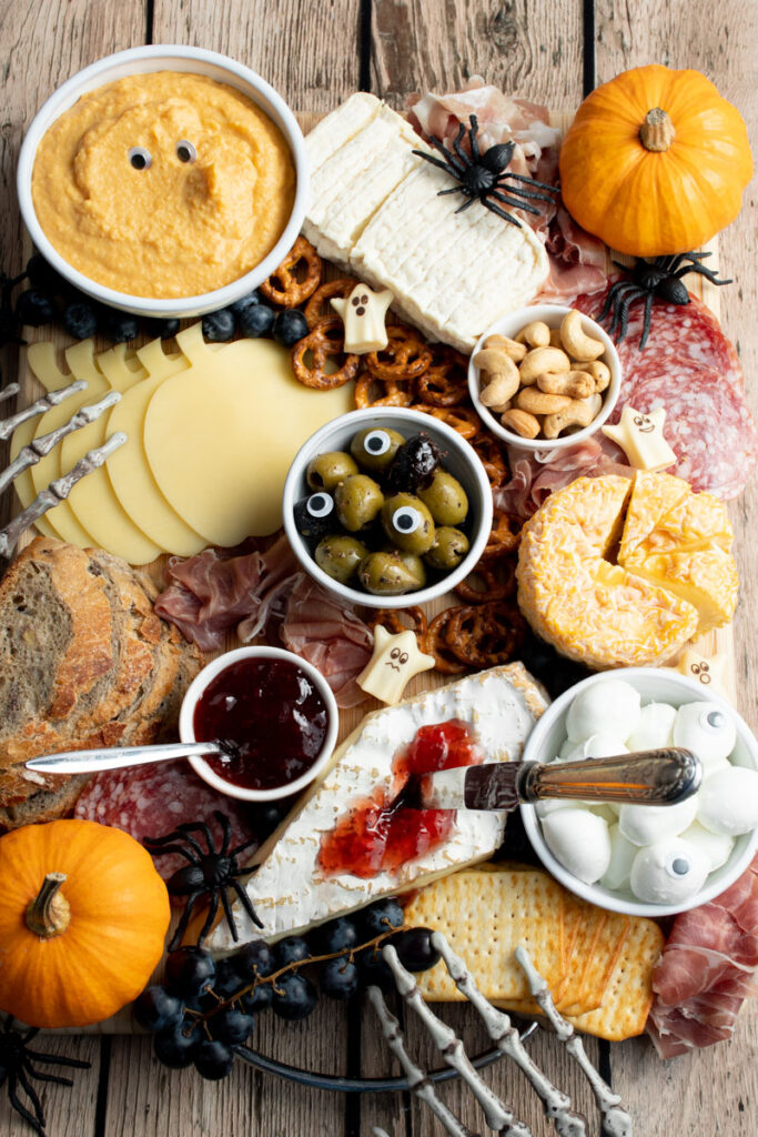 Halloween charcuterie board with cheeses, charcuterie, pumpkins, coffin of cheese, olives with eyes, skeletons hands, spiders...