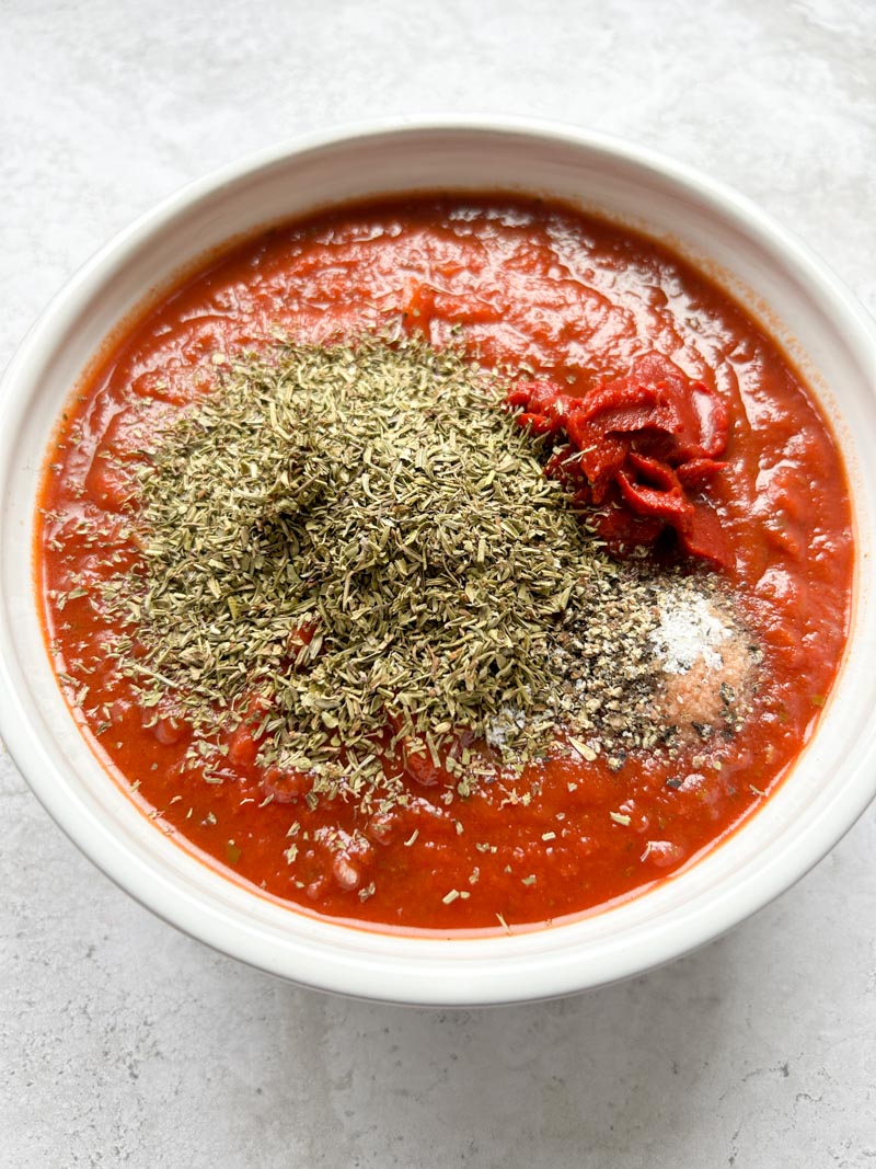 Sauce tomate, thym, concentré de tomates, sel et poivre dans un bol blanc.