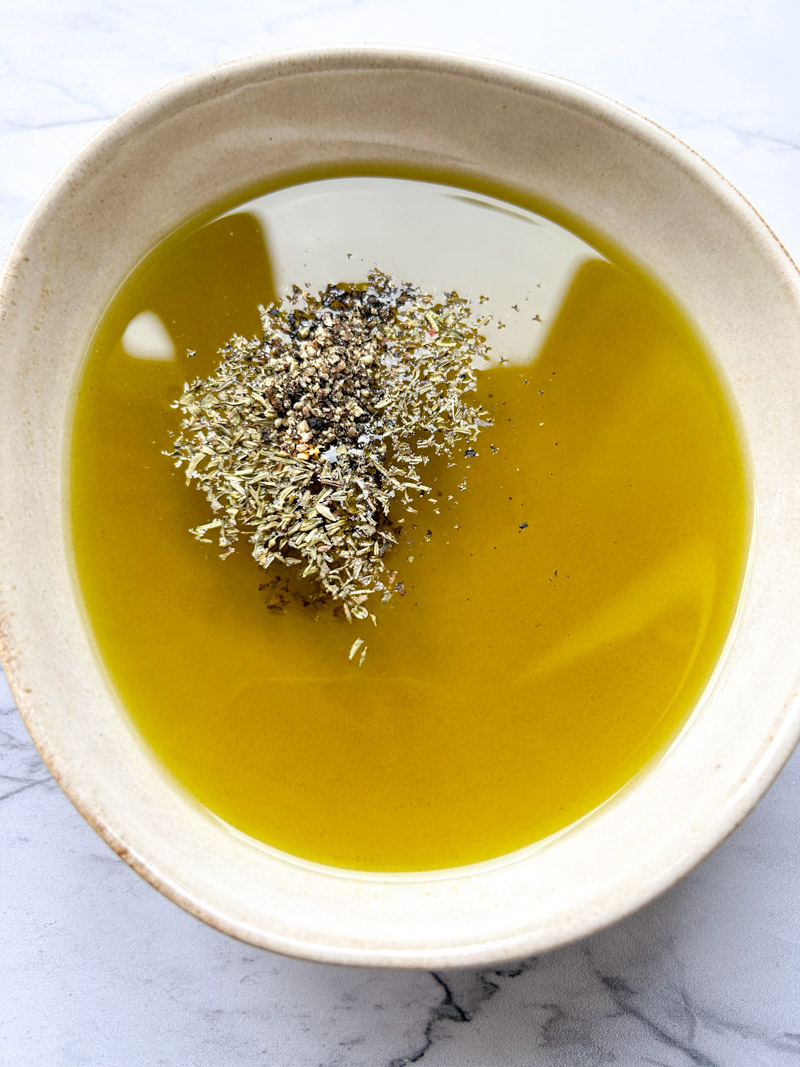 Olive oil in a bowl with salt, pepper, red chili flakes and thyme.