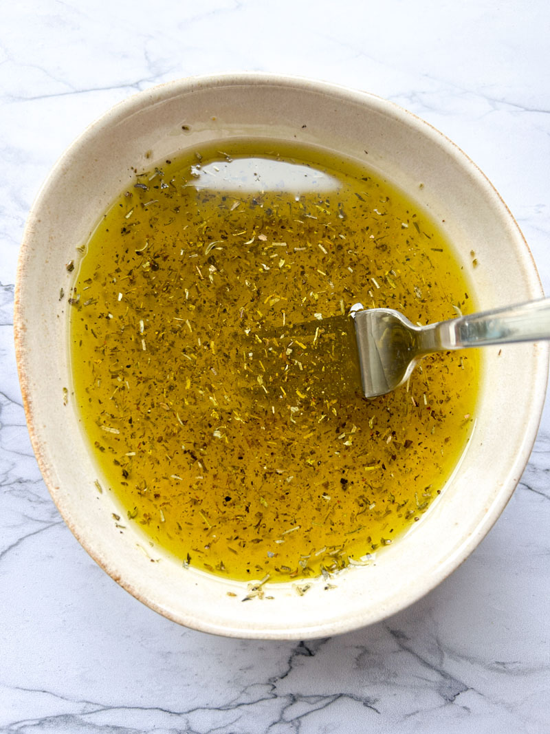 Huile d'olive dans un bol mélangée avec du sel, du poivre, flocons de piment et thym.