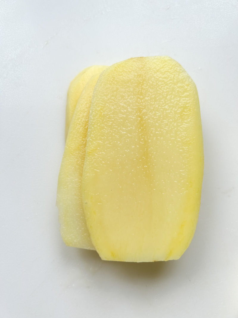 Frites de pommes de terre les unes sur les autres, sur une planche à découper blanche.