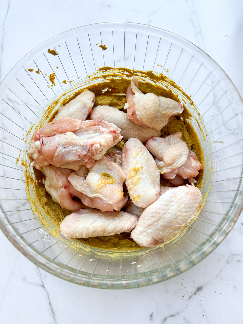 Wings de poulet ajoutées à la marinade Tandoori dans un bol transparent.