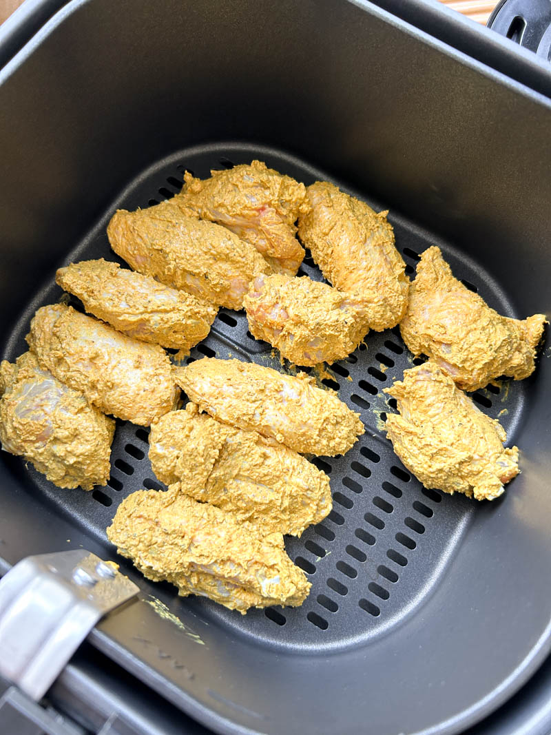 Ailes de poulet enrobées de marinade Tandoori dans le panier du Air Fryer.