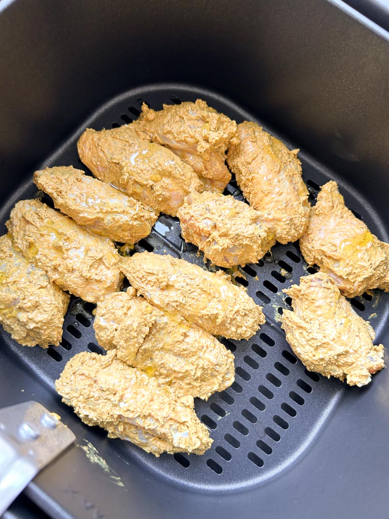 Wings de poulet enrobées de marinade tandoori avec un filet d'huile d'olive dans le panier du Air Fryer.